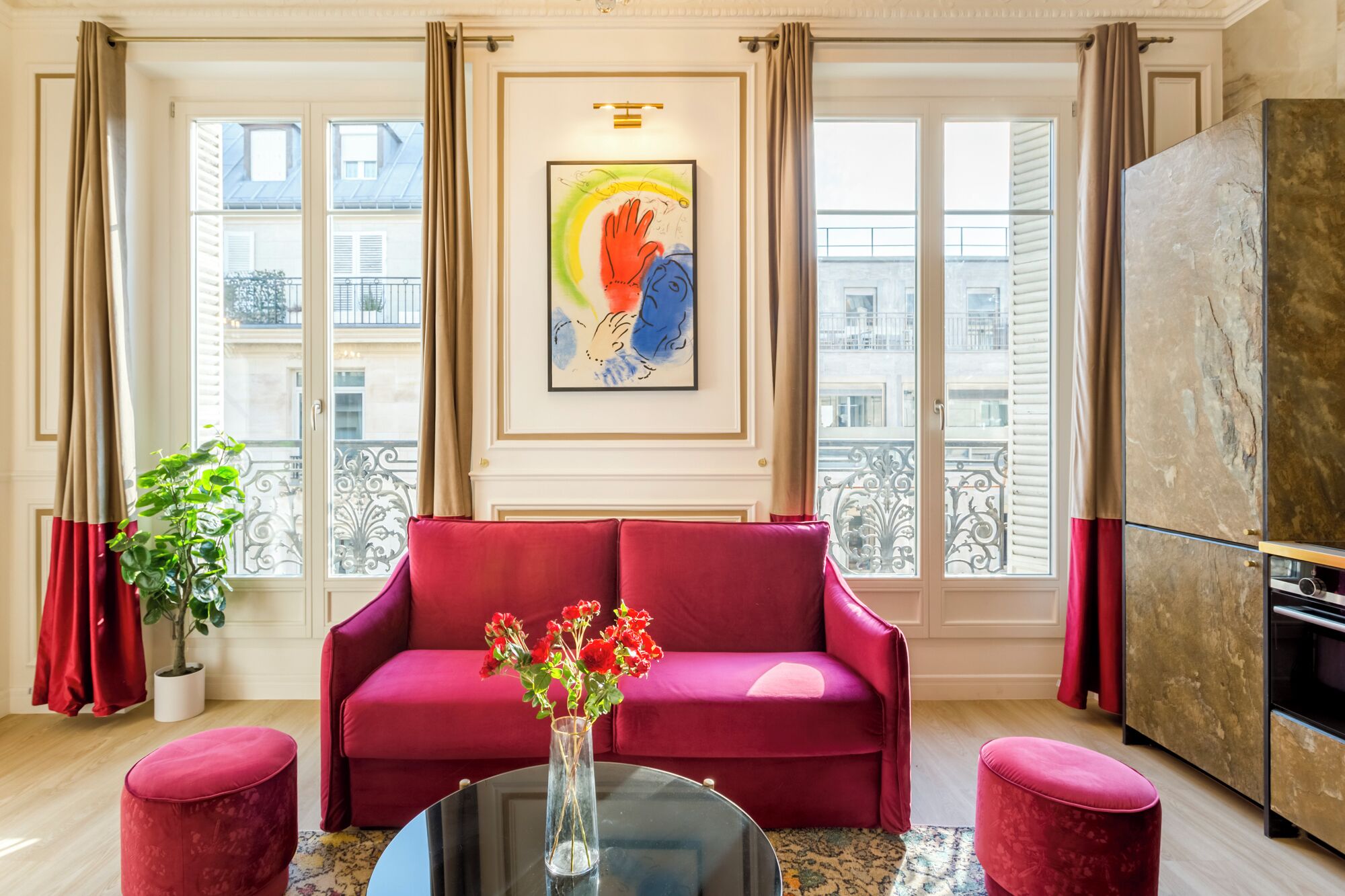 A living room with a red sofa, a glass coffee table with flowers, and a painting above the sofa.