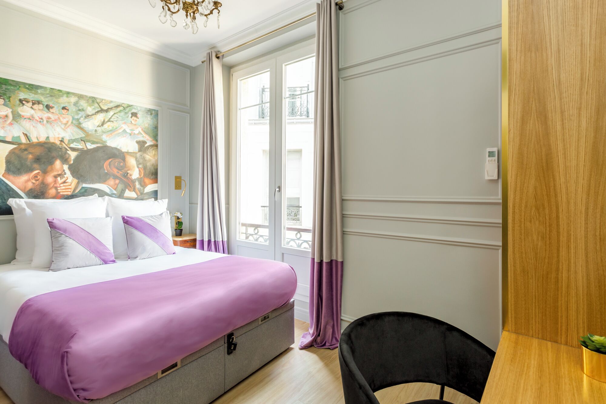 A bedroom with a bed, a desk, a chair, a window with curtains, a painting on the wall, and a chandelier.