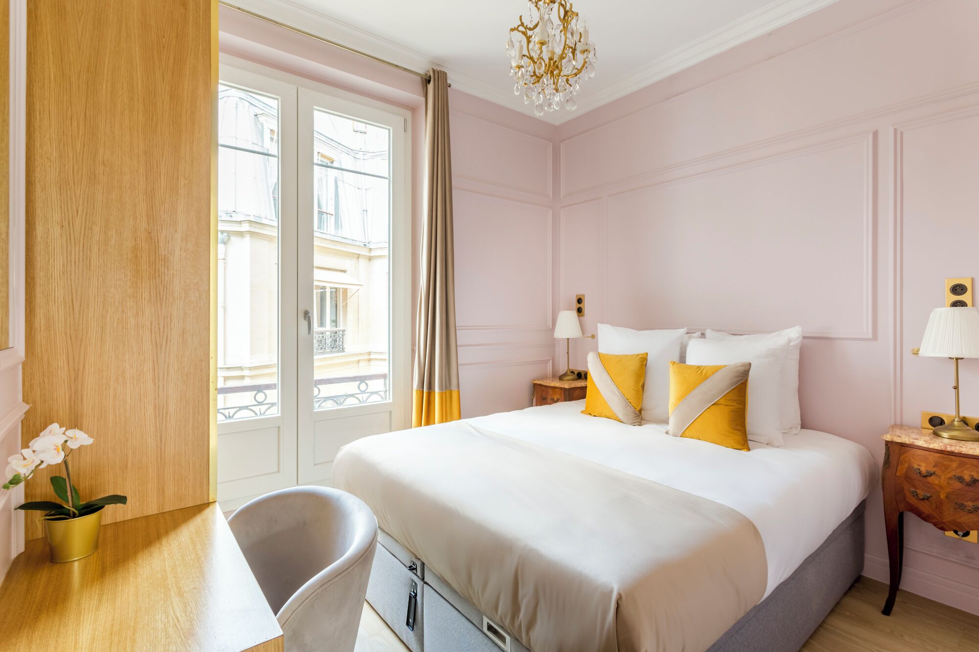 Una habitación de hotel con una cama grande, un escritorio, una silla y vistas a la ciudad a través de un ventanal amplio.