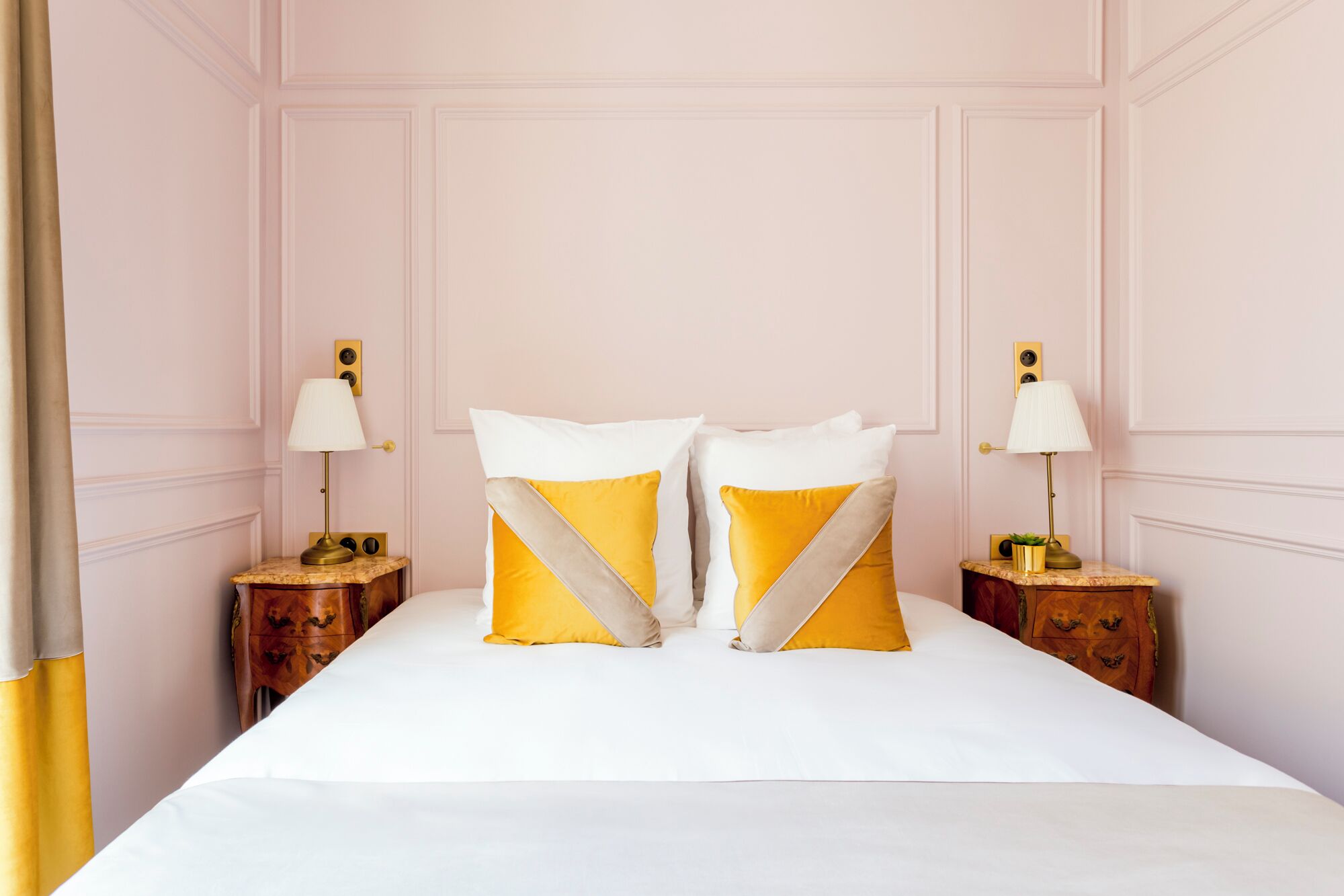 A hotel room with a large bed, two bedside tables with lamps, and a wooden nightstand.