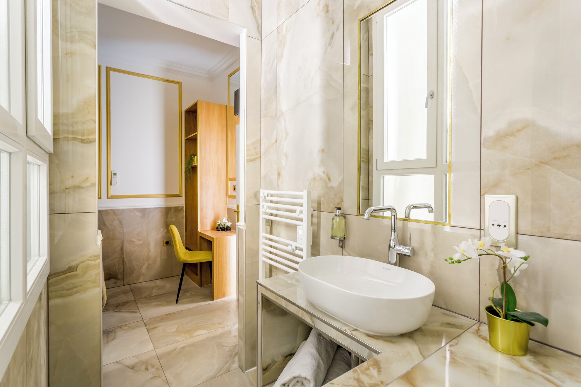 Un baño moderno con un lavabo blanco grande, un espejo y una silla amarilla.
