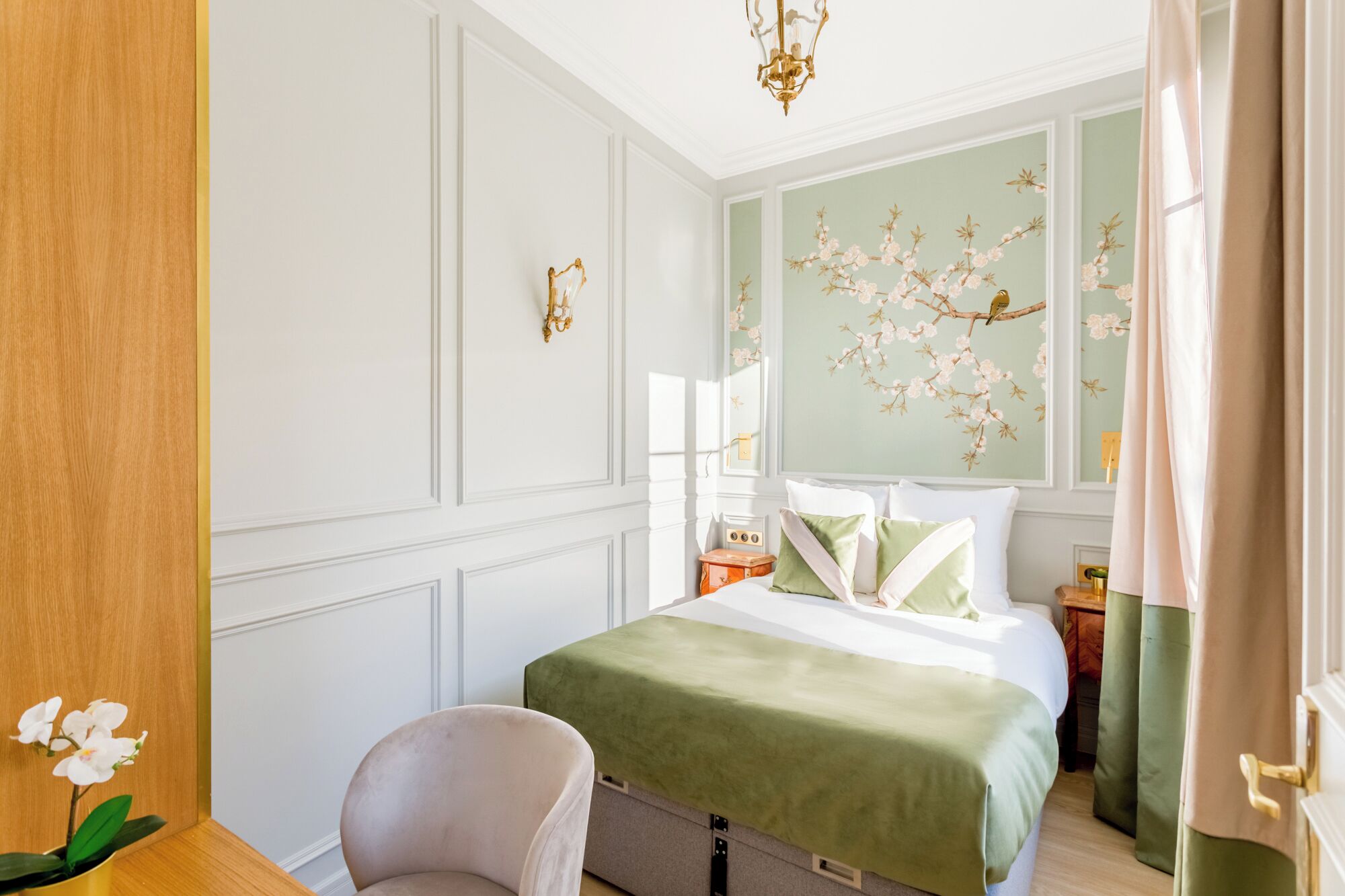A bedroom with a bed, a chair, a nightstand, and a wall-mounted lamp.
