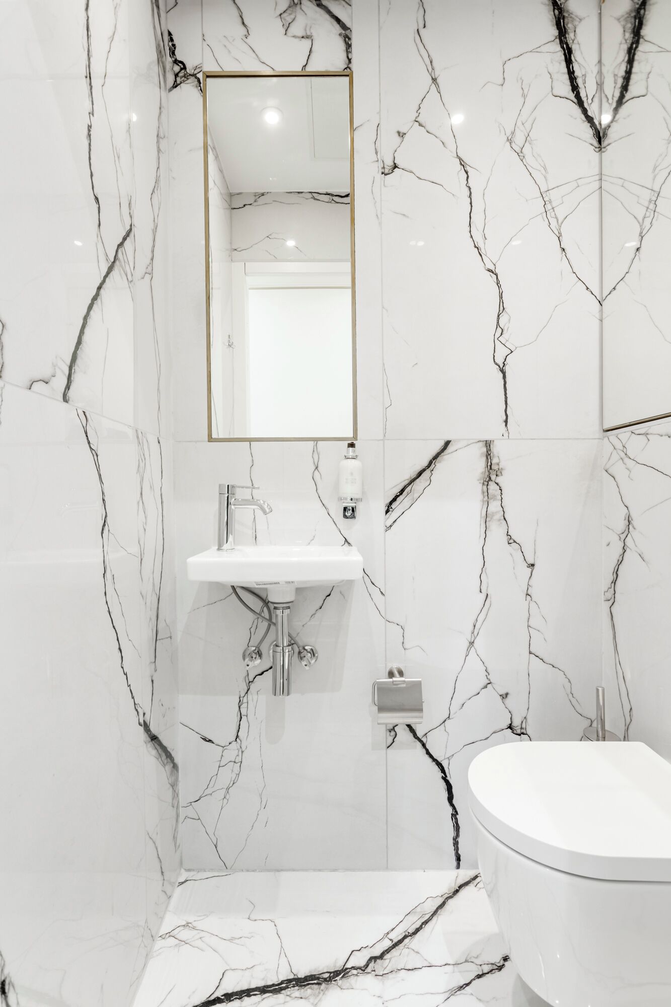 A bathroom with a white marble wall, a sink, a toilet, and a mirror.