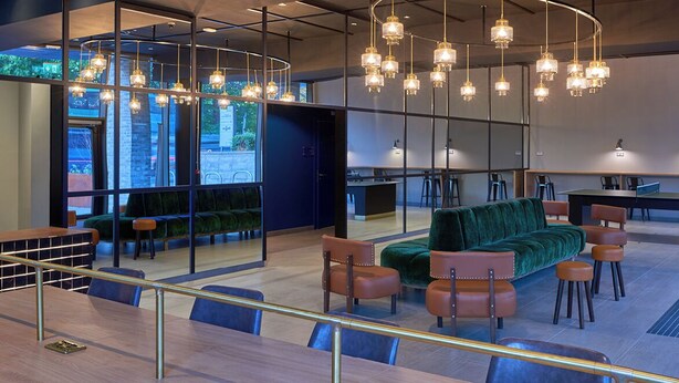 A modern lounge area with a green sofa, brown chairs, and hanging pendant lights. - Student Only Cumberland Place (Southampton)