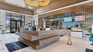 Uma área de recepção moderna com um balcão de madeira, um painel de menu digital e vista para a área externa.