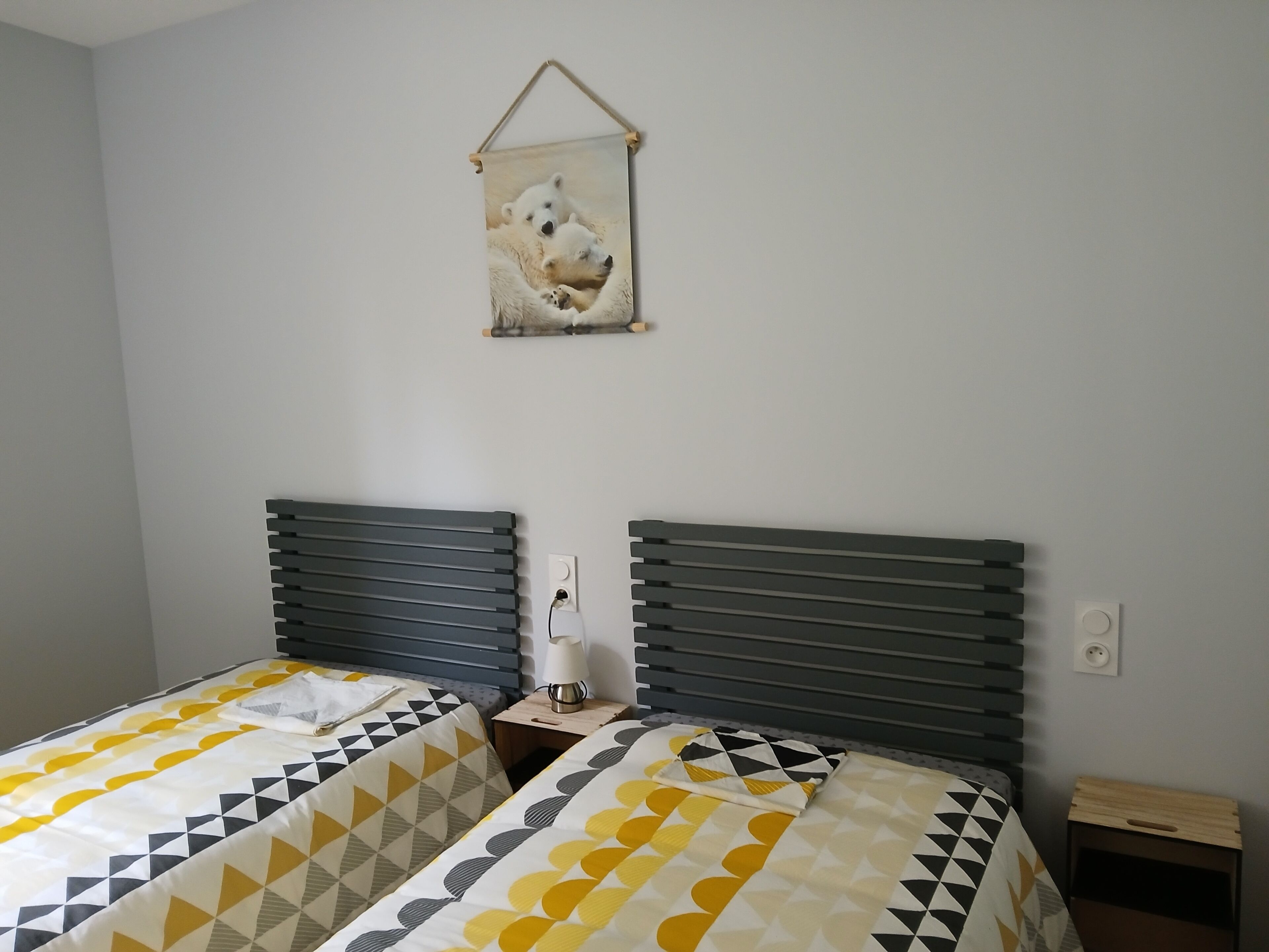 Ein Schlafzimmer mit zwei Betten, jeweils mit einem geometrisch gemusterten Überwurf, einem Nachttisch mit Lampe und einem Wandbild von Eisbären.