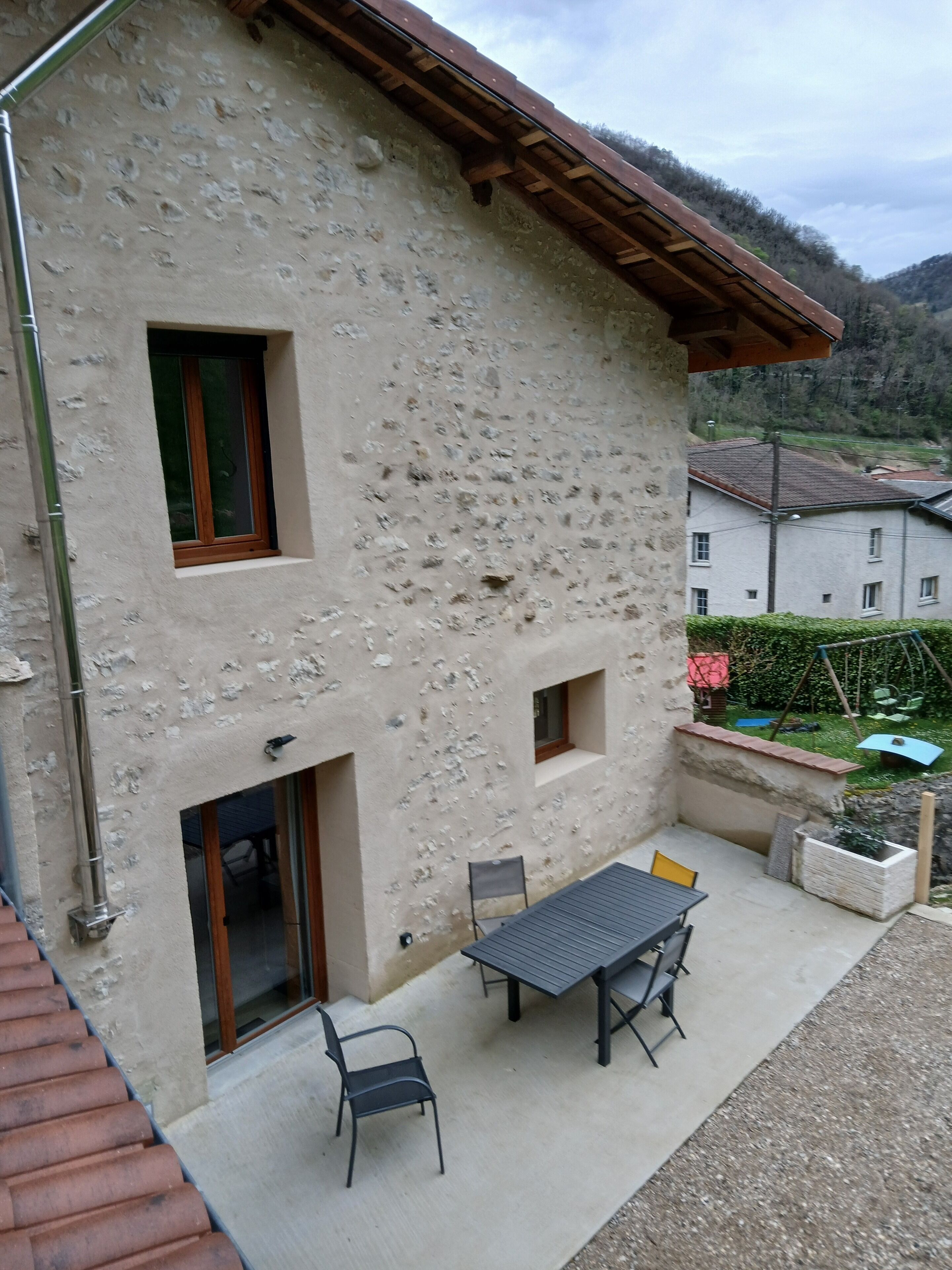 A stone house with a patio, a table, and two chairs.