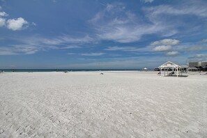 Een breed zandstrand met een heldere lucht en enkele wolken.