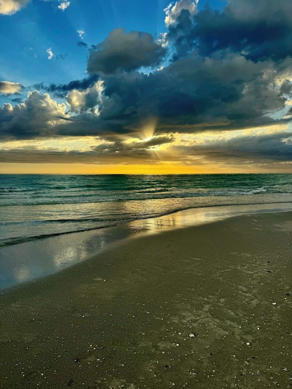A beach with a sunset, waves, and a cloudy sky.