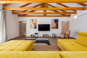 Una sala de estar moderna con vigas de madera, un televisor de pantalla plana, dos sofás amarillos y obras de arte en las paredes.
