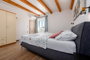 A bedroom with a bed, a wardrobe, a window with curtains, and a wall-mounted lamp. - Villa Rosea Domus ZadarVillas (Podlug)