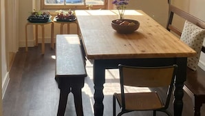 Un coin repas avec une table en bois, un banc et des chaises. Une fenêtre offre une vue sur la rue.