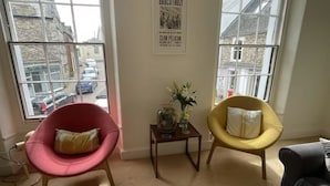 Une pièce comprenant deux fauteuils, une petite table avec un vase et une affiche accrochée au mur.