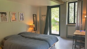 A bedroom with a bed, a desk, a chair, a window, and artwork on the wall.