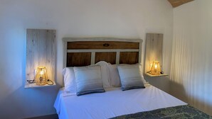 A bedroom with a wooden headboard, white bedding, and two wall-mounted lamps.