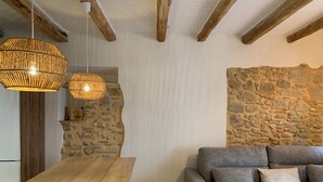 A cozy living area with a stone wall, wooden beams, a grey sofa, and two wicker pendant lights.