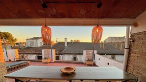 An outdoor patio with a table and chairs, two hanging lanterns, and a view of buildings in the background.