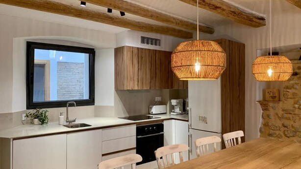 A modern kitchen with white cabinets, a wooden dining table, and two hanging wicker light fixtures.