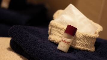 Una botella de champú de hotel y una toalla blanca en una cesta con textura.