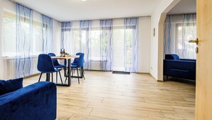 A spacious room with a wooden floor, a dining table with chairs, a sofa, and large windows with sheer curtains. - New vacation apartment in Sigmaringen, 15 minutes' walk to the pedestrian zone. (Sigmaringen)