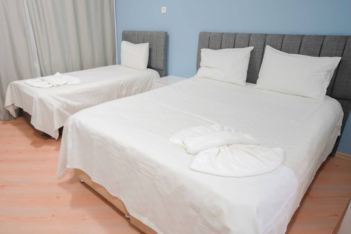 A hotel room with two single beds and one double bed, all with white linens and pillows.