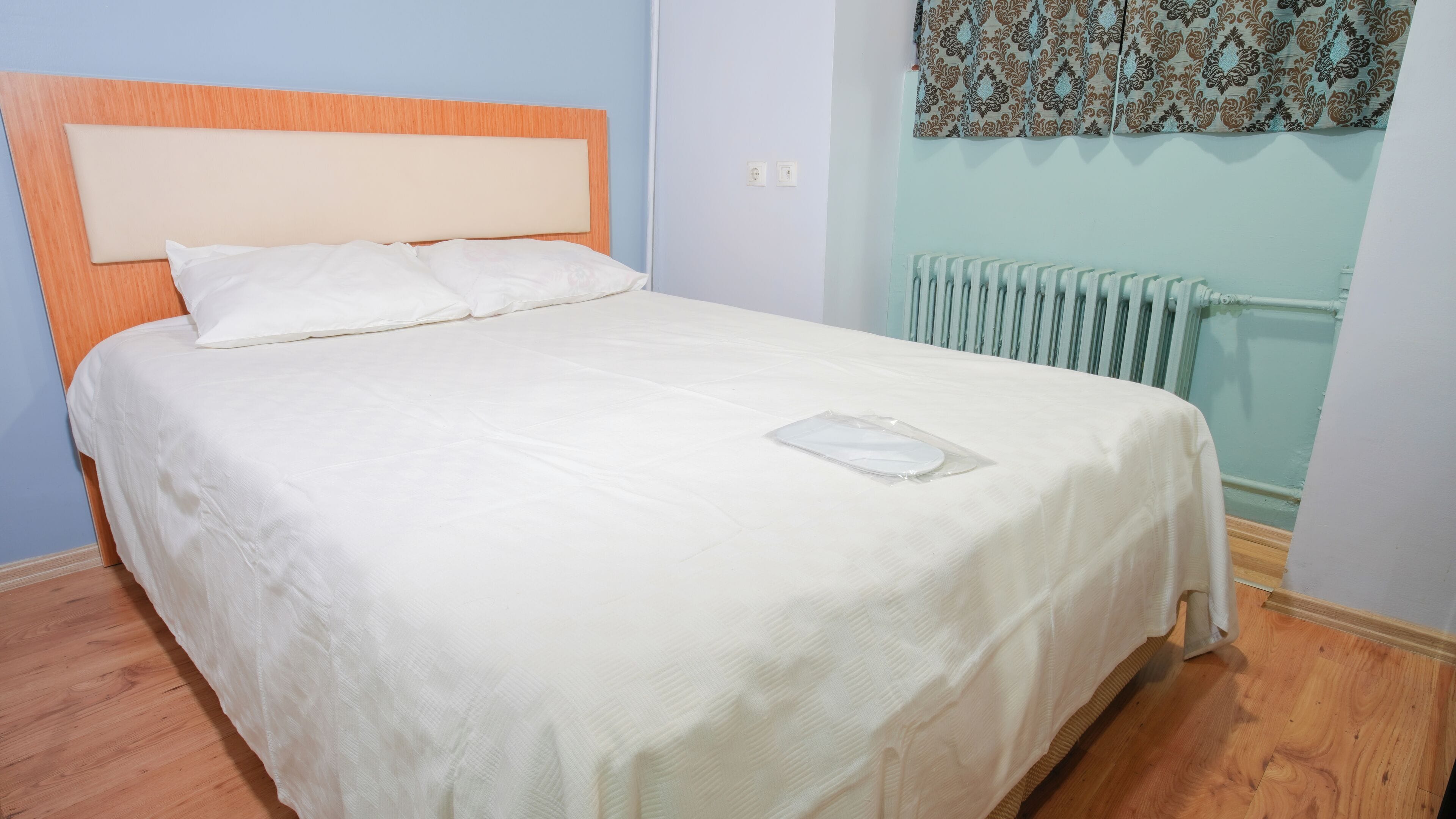 A neatly made bed with a white bedspread and pillows, a wooden headboard, and a radiator in the background.