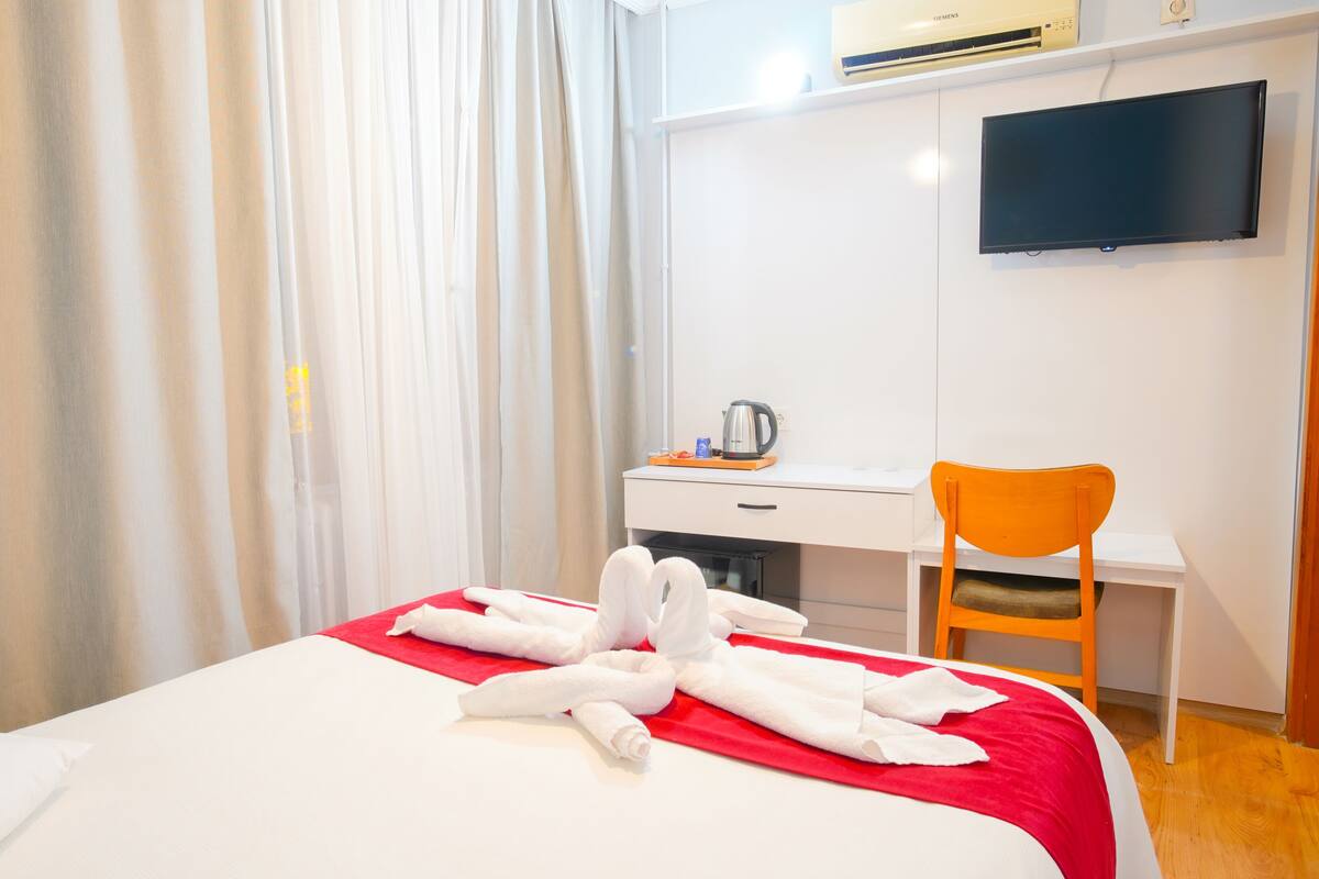 A hotel room with a bed, a desk, a chair, and a television on the wall.