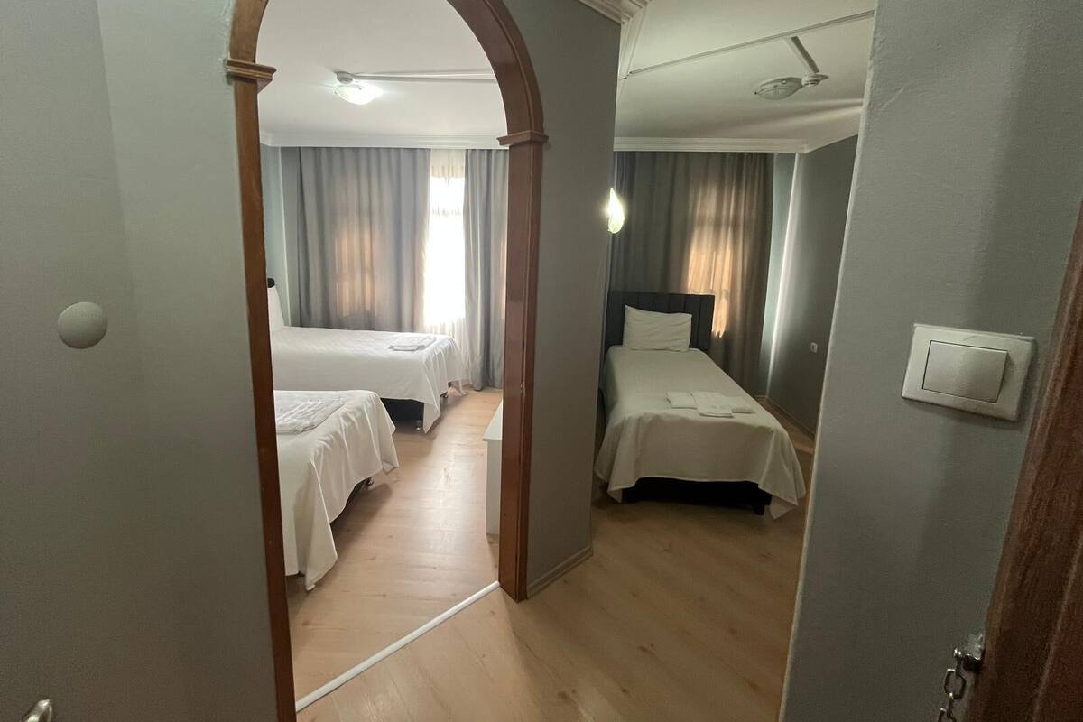 A hotel room with two beds, a wooden floor, a ceiling fan, and a light fixture.
