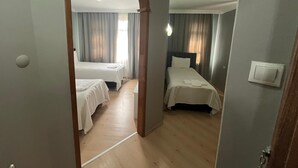 Quarto de hotel com duas camas, piso de madeira, ventilador de teto e luminária.