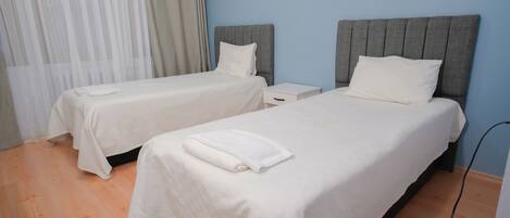 Ein Hotelzimmer mit zwei Einzelbetten, jeweils mit grauer Kopfteil und weißer Bettwäsche.