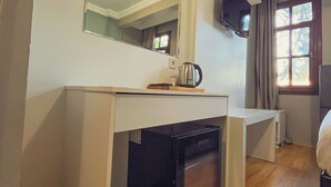 Quarto compacto com cozinha americana, um espelho grande, televisão fixada na parede e uma janela com cortinas.