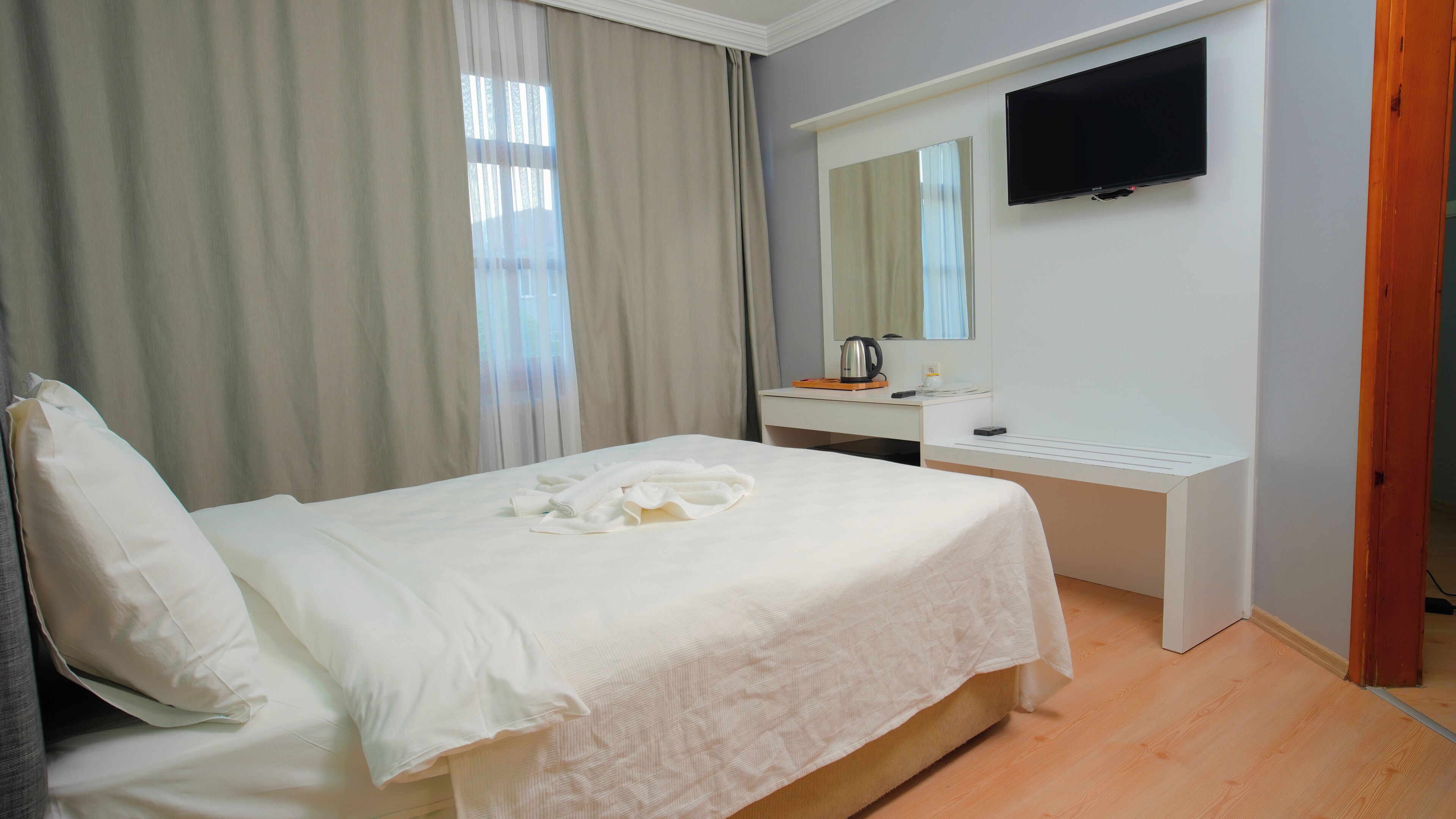 A hotel room with a bed, a desk, a television, and a window with curtains.