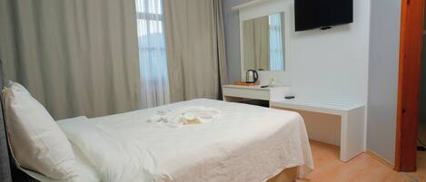 A hotel room with a bed, a desk, a television, and a window with curtains.