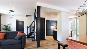 Een moderne woonkamer met een donkere bank, een houten eettafel en een trap die naar een keuken leidt.