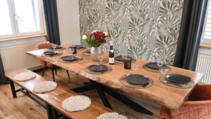 Een eettafel gedekt met zwarte borden, witte placemats en een vaas met bloemen.