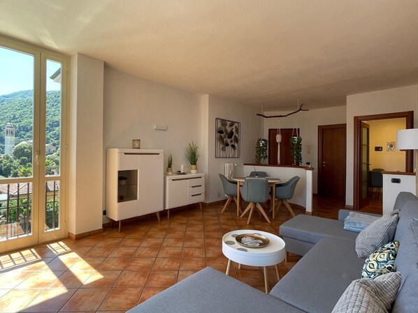 A modern living room with a sofa, a dining table with chairs, and a kitchen area with cabinets and a countertop.