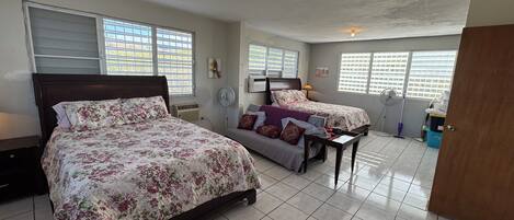 A bedroom with two beds, a fan, and a window with blinds.