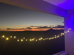 Une pièce décorée avec un tableau représentant un paysage au coucher du soleil, accroché au mur, une guirlande lumineuse et un luminaire fixé au plafond.