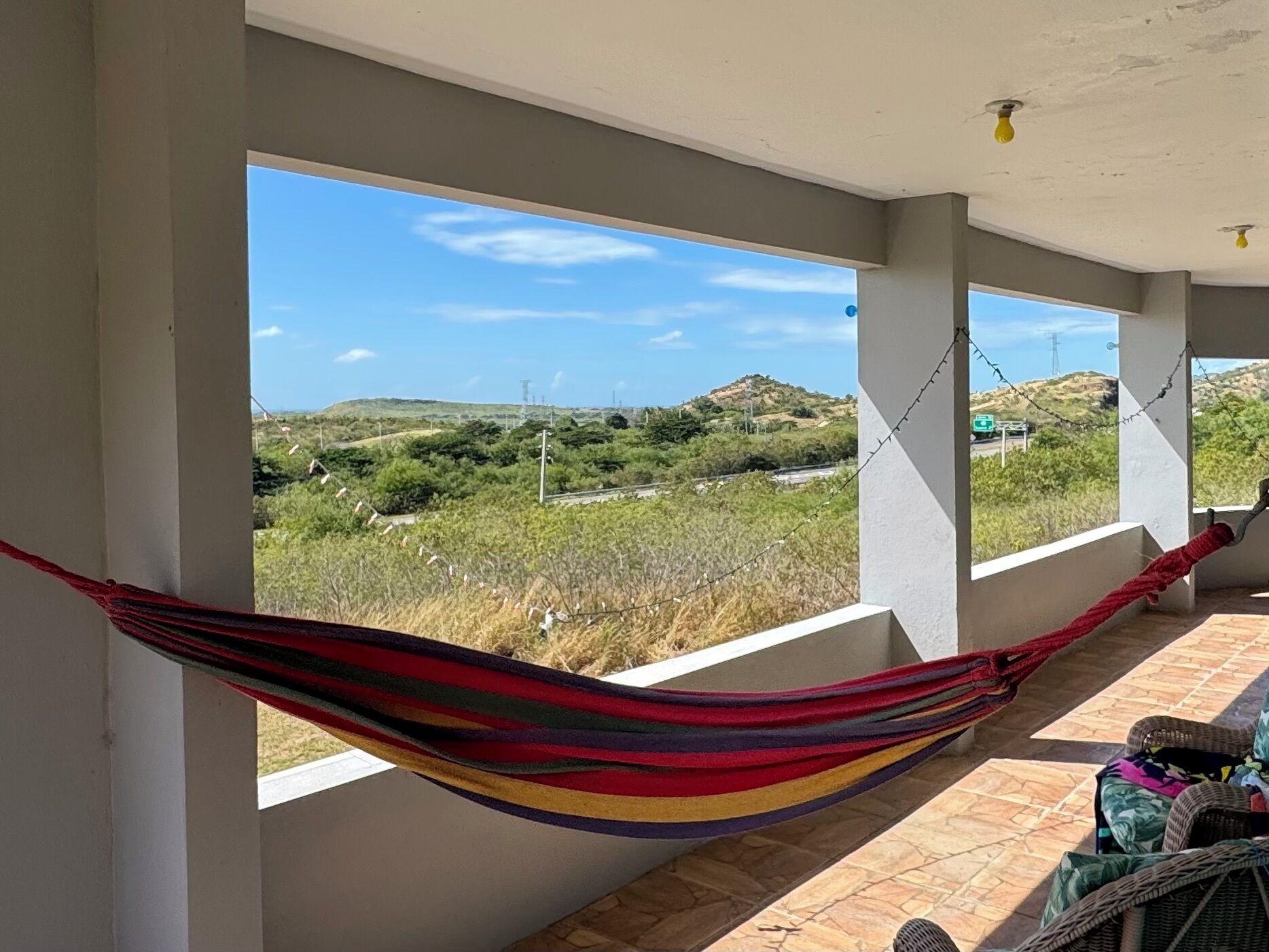 A room with a hammock, large windows, and a view of a hilly landscape.