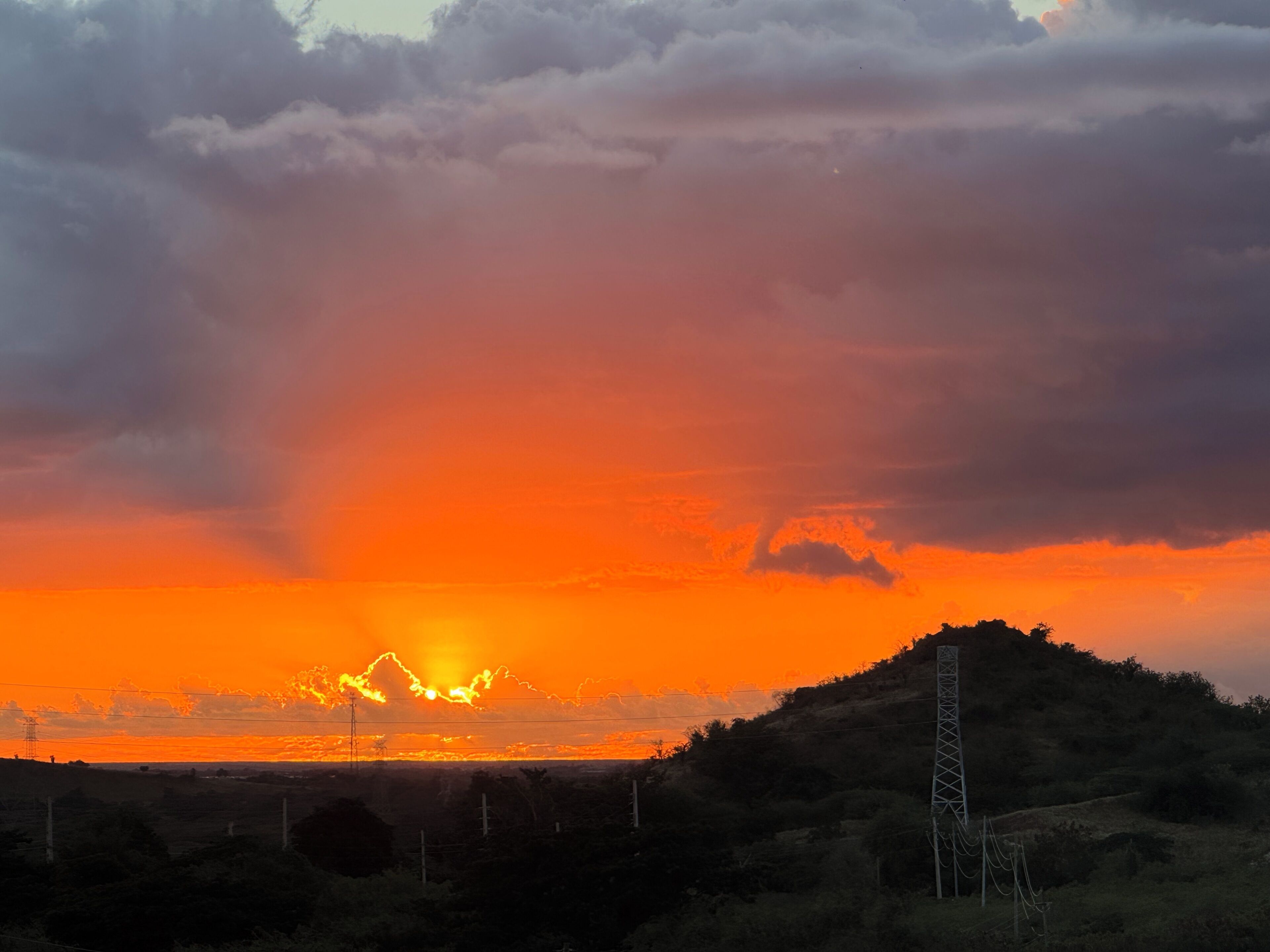 A sunset over a hilly landscape with a power line tower.