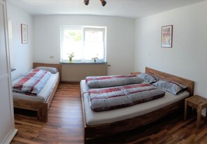 Une chambre avec deux lits simples et un grand lit double, un plancher en bois, un radiateur, une fenêtre avec vue et une petite table de chevet.