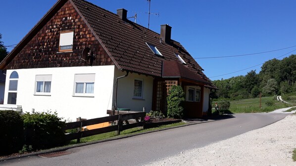 Une maison à deux étages avec un toit en pente, un petit garage attenant et une allée gravillonnée.