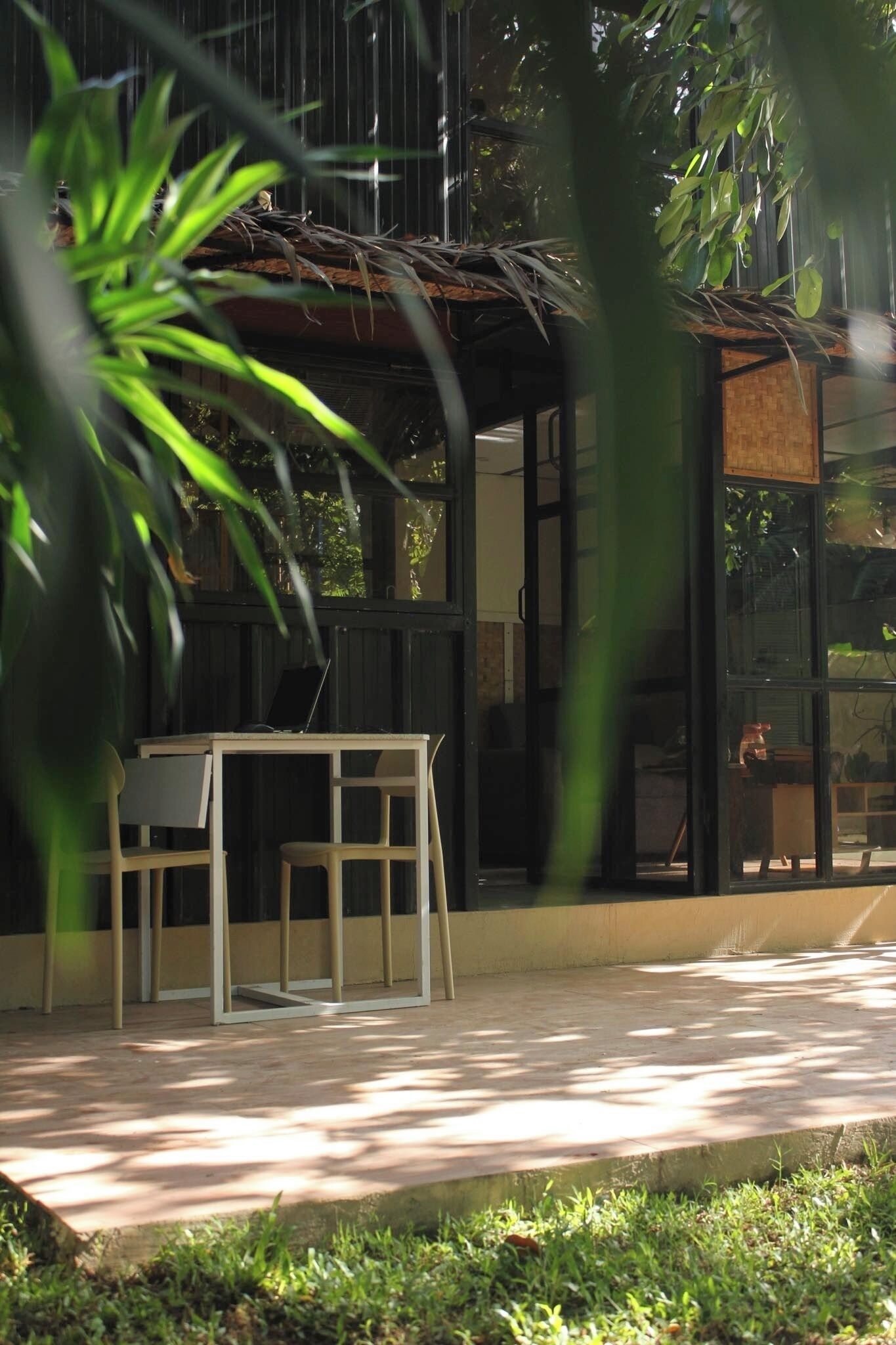 A modern outdoor seating area with a table and chairs, surrounded by greenery and a glass enclosure.