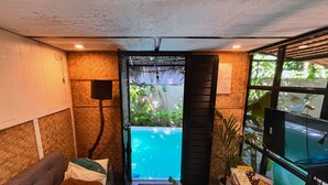 Une pièce confortable avec vue sur une piscine, un canapé, une petite table avec une plante et un téléviseur posé sur un meuble.