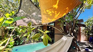Un hamac installé dans un endroit ombragé, une piscine et une végétation luxuriante tout autour.