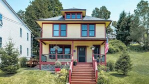 A two-story house with a front porch, a small staircase leading to the entrance, and a flag on the right side. - Historic Sears Roebuck House (Thomas)