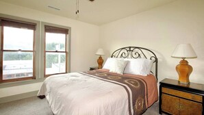 A bedroom with a bed, two bedside lamps, a nightstand, a ceiling fan, and two windows. - Historic Sears Roebuck House (Thomas)