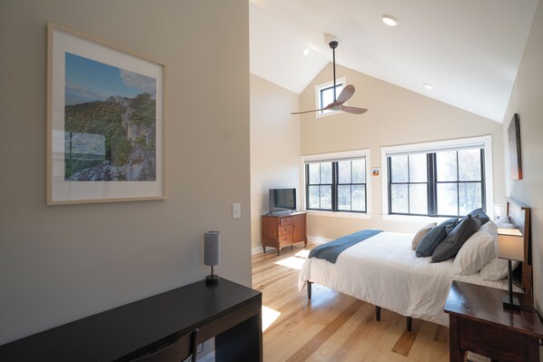 A bedroom with a bed, a desk, a TV, and a ceiling fan.
