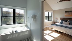 Ein Schlafzimmer mit einem großen Bett, einem Nachttisch, einem Fenster mit Blick auf Bäume und einem Deckenventilator.