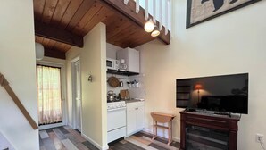 Eine kleine Küche mit weißen Schränken, einer Mikrowelle und einem Herd. Ein Holztisch und ein Fernseher auf einem Schrank stehen dort.